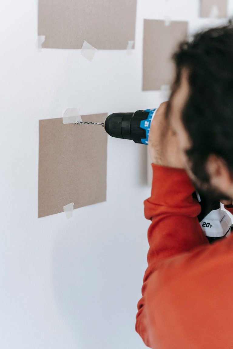 A man using a power drill on a wall, focusing on precision and safety during home renovation. Un homme utilisant une perceuse électrique sur un mur, en se concentrant sur la précision et la sécurité pendant la rénovation domiciliaire.