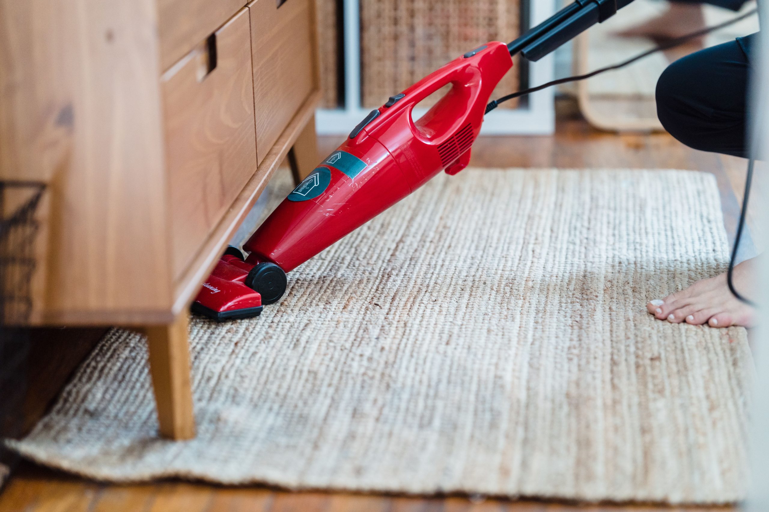 Personne utilisant aspirateur rouge sous meuble tapis