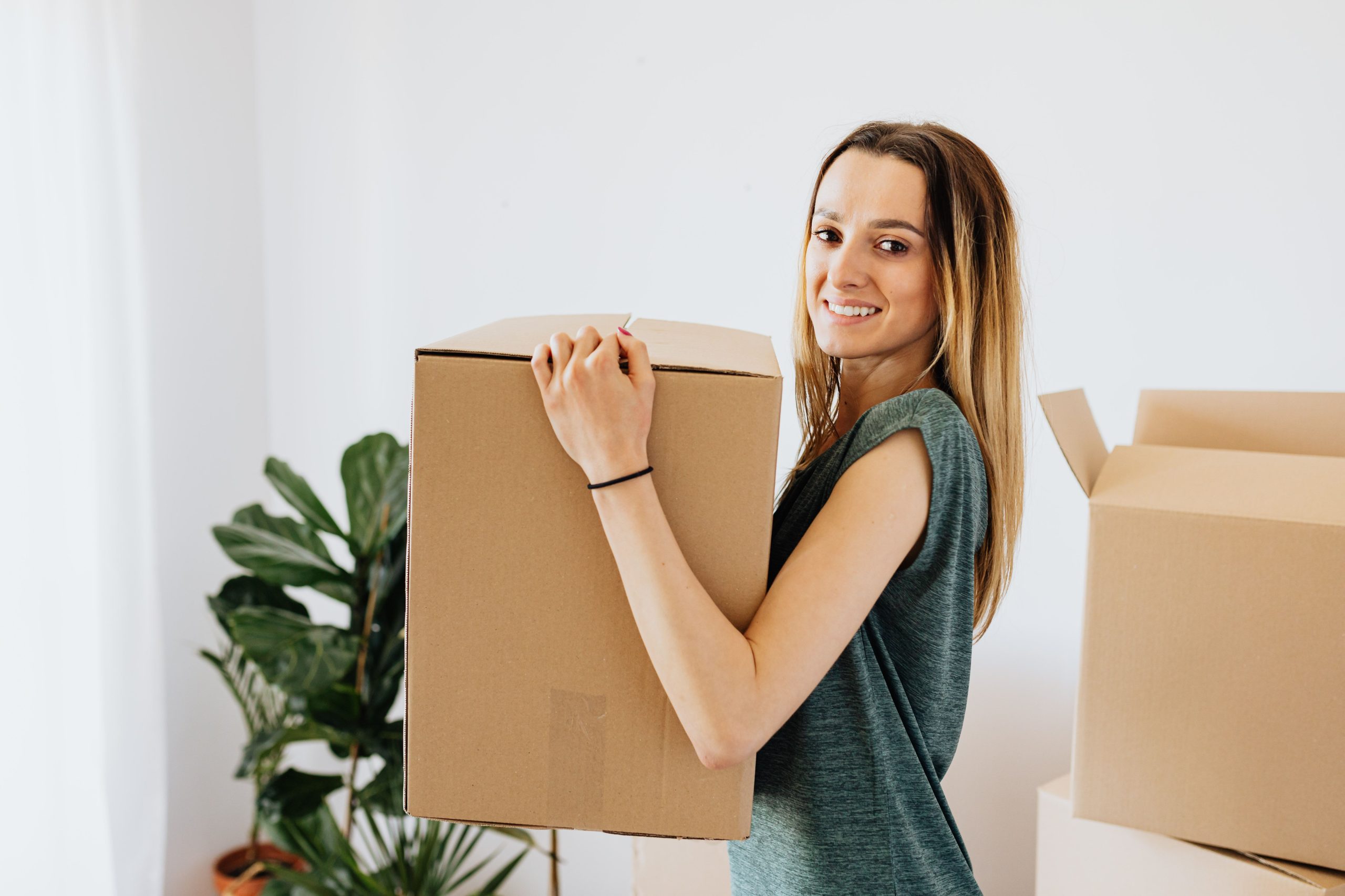 Femme souriante en chemise verte portant carton déménagement